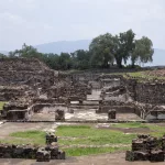 Ruinen einer antiken Wohnanlage in Teotihuacán mit Baumgruppen und grünen Hügeln im Hintergrund.
