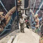 Street Art in der Comuna 13 Medellín – Wandgemälde mit riesigen Händen und Besucherin in den Gassen