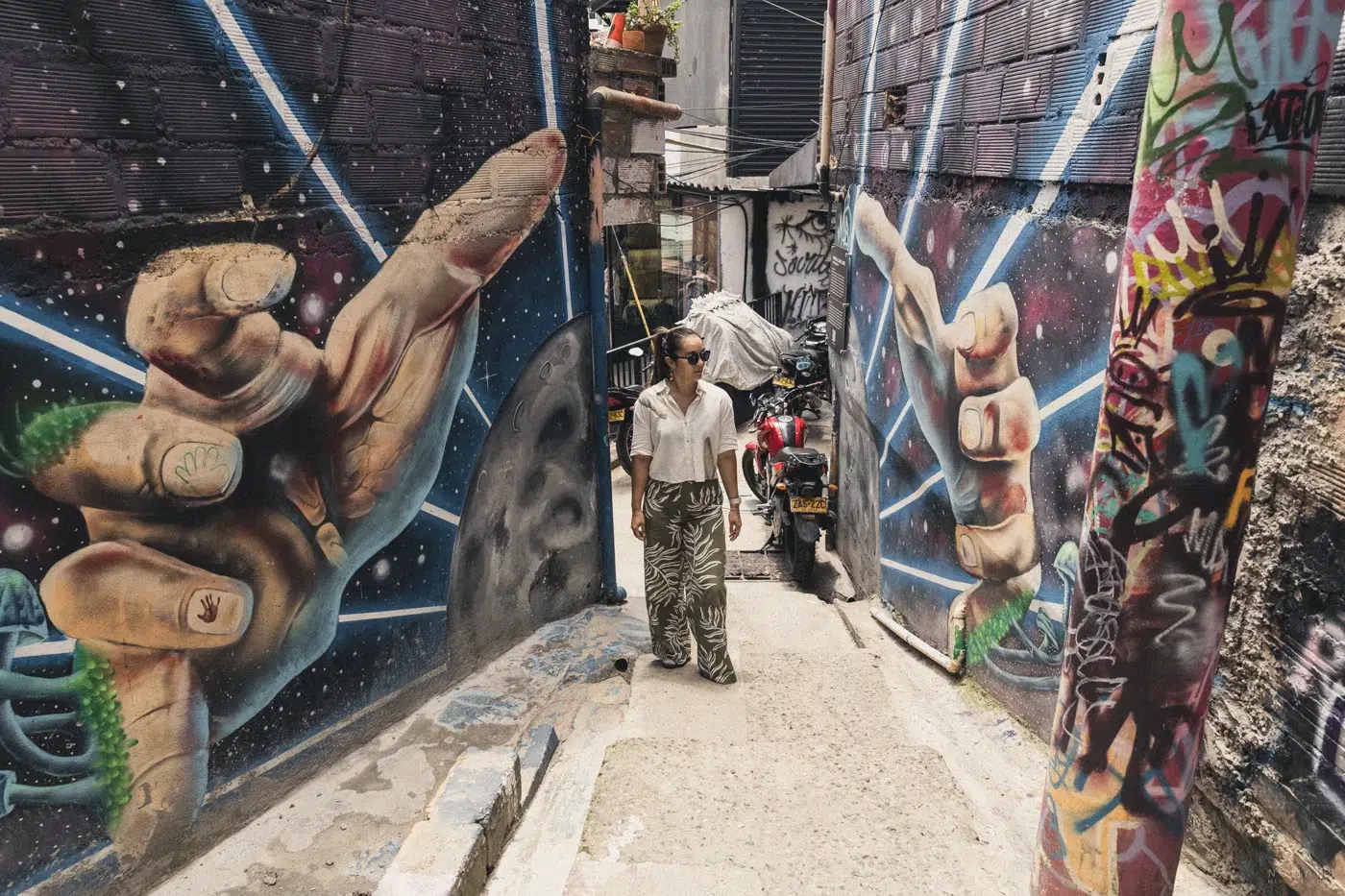 Street Art in der Comuna 13 Medellín – Wandgemälde mit riesigen Händen und Besucherin in den Gassen