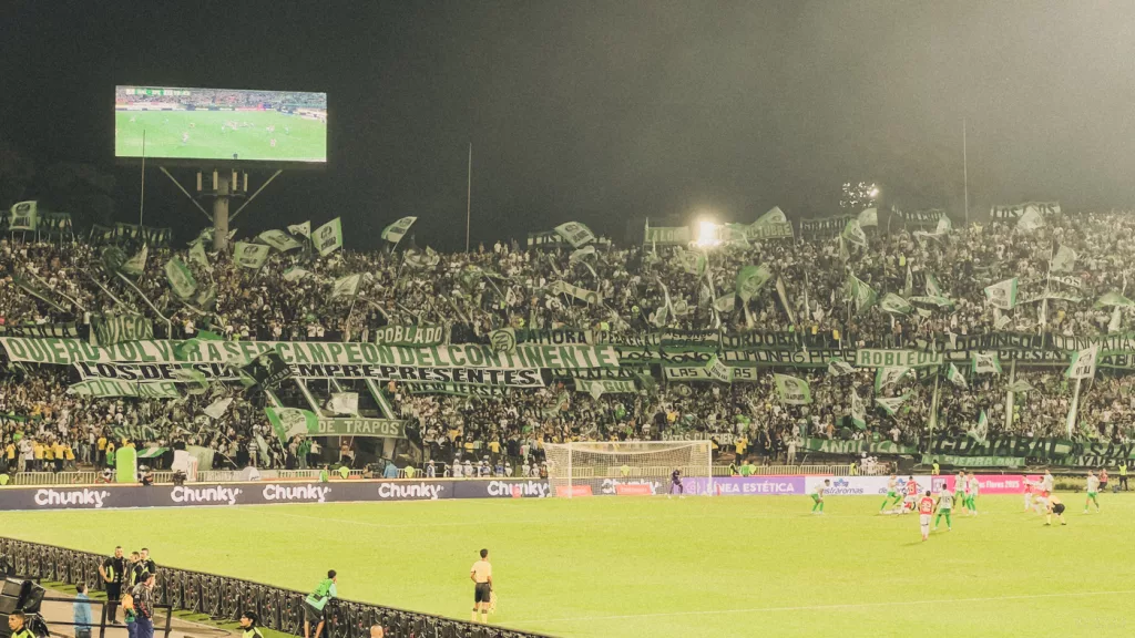 Fußballspiel von Atlético Nacional im Estadio Atanasio Girardot in Medellín mit voller Fankurve, grünen Bannern und ausgelassener Stimmung.