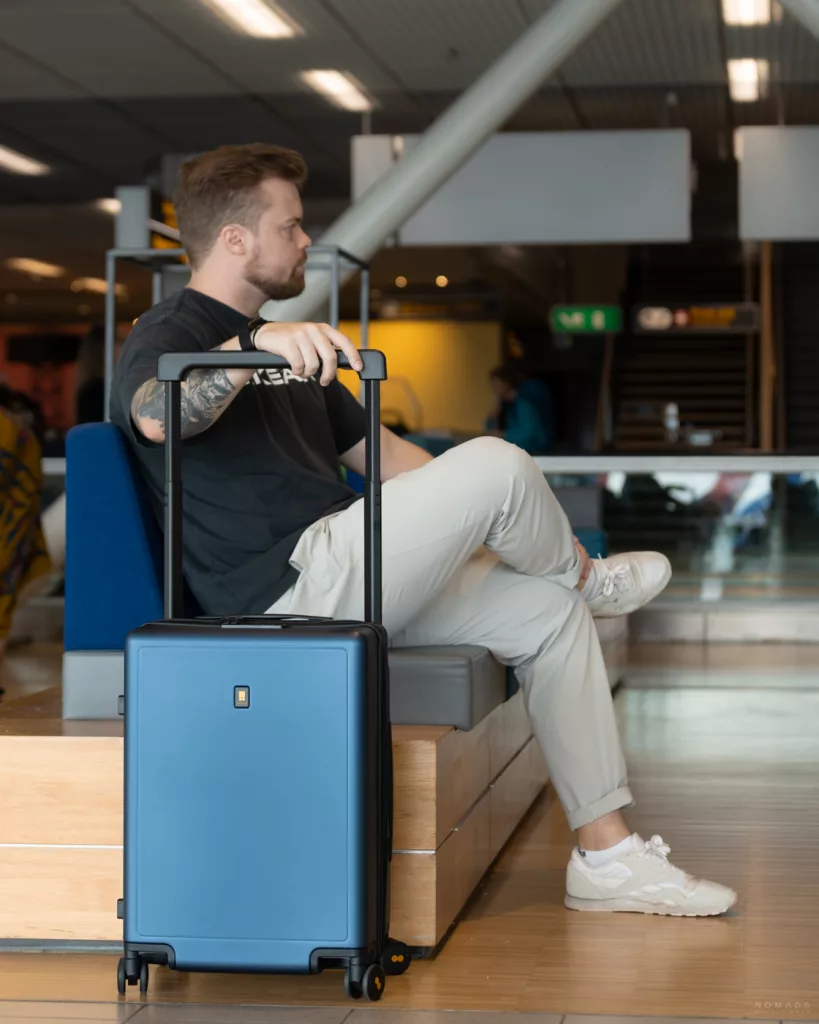 Reisender sitzt am Flughafen und hat den blauen Level8 Handgepäckkoffer neben sich stehen.