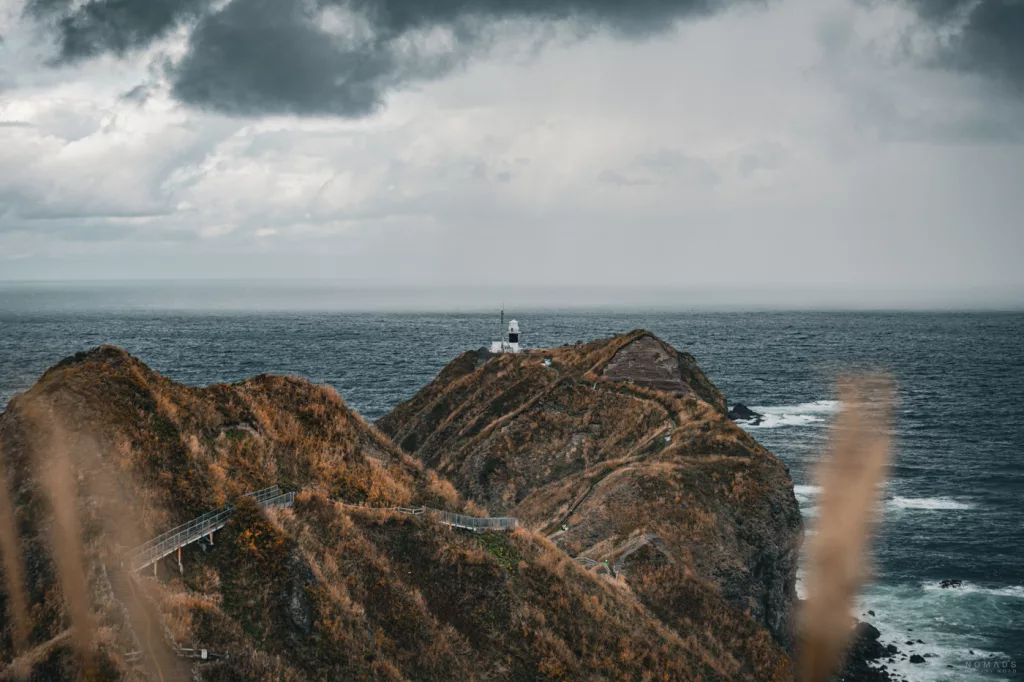 Blick auf das Kap Kamui mit seinem Leuchtturm, umgeben von steilen Klippen und dem wilden Meer unter dunklen Regenwolken.