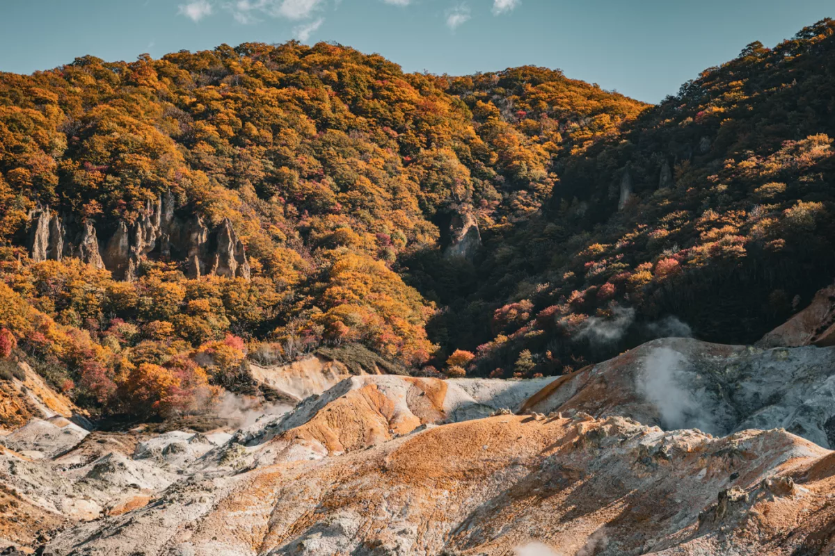 Blick auf das sogenannte Höllental (Jigokudani) bei Noboribetsu, wo dampfende Schwefelquellen auf farbenfrohe Herbstwälder treffen.
