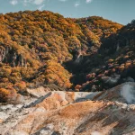 Blick auf das sogenannte Höllental (Jigokudani) bei Noboribetsu, wo dampfende Schwefelquellen auf farbenfrohe Herbstwälder treffen.