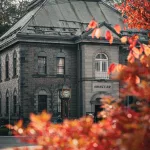 Historisches Backsteingebäude mit Dampf-Uhr in Otaru, eingerahmt von herbstlich gefärbtem Laub im Vordergrund