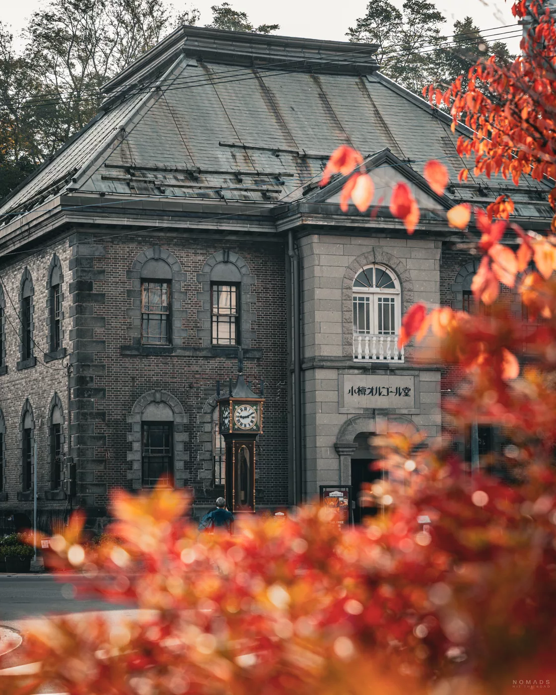 Historisches Backsteingebäude mit Dampf-Uhr in Otaru, eingerahmt von herbstlich gefärbtem Laub im Vordergrund