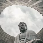 Blick durch die runde Öffnung eines Betongewölbes auf die monumentale Buddha-Statue im Makomanai Takino Cemetery in Sapporo.