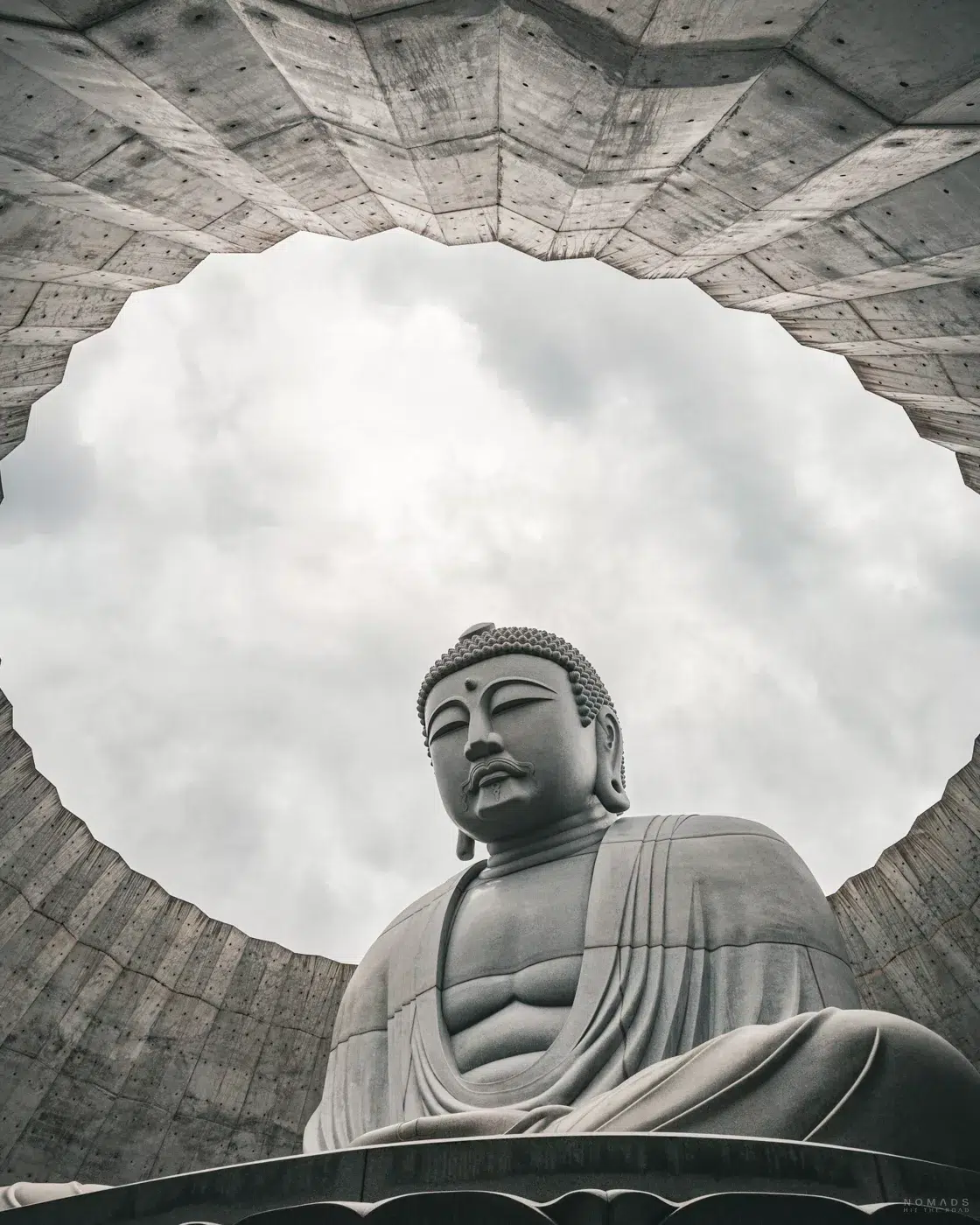 Blick durch die runde Öffnung eines Betongewölbes auf die monumentale Buddha-Statue im Makomanai Takino Cemetery in Sapporo.