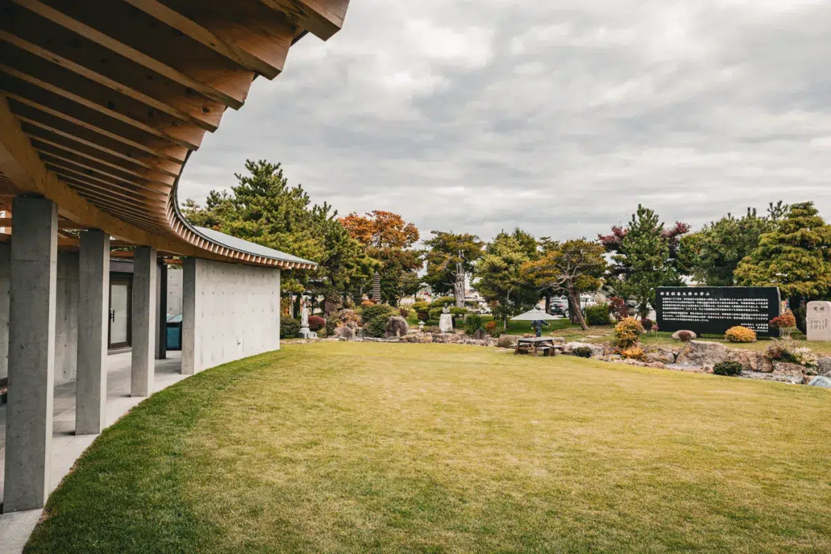 Ansicht eines überdachten Ganges mit geschwungener Dachkonstruktion, der in den japanischen Garten des Makomanai Takino Cemetery führt.