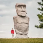 Große steinerne Moai-Statue mit einer Person in roter Jacke davor im Makomanai Takino Cemetery – ein ungewöhnlicher Anblick in Japan.