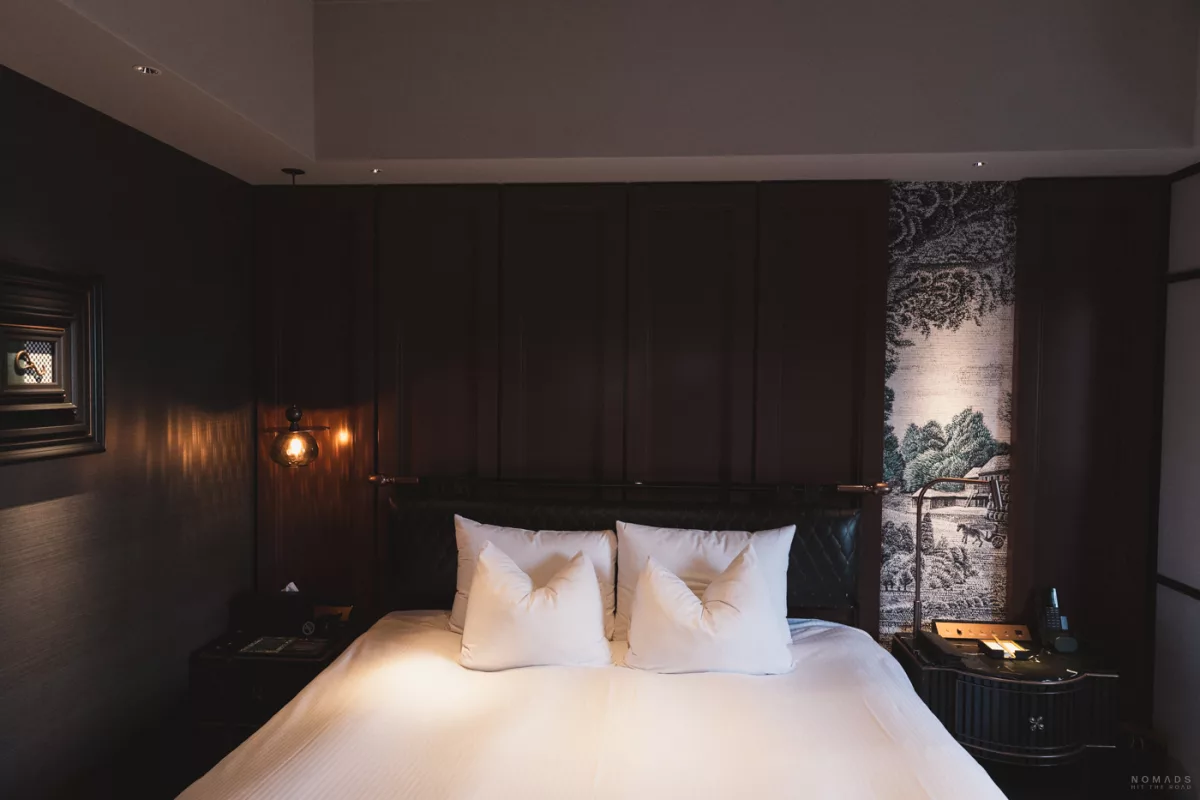 Elegantes Hotelzimmer im Hotel Sosei Sapporo – MGallery Collection mit einem großen Bett, weißen Kissen, dunkler Holzverkleidung und stilvoller japanischer Wandkunst im Hintergrund.