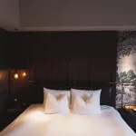 Elegantes Hotelzimmer im Hotel Sosei Sapporo – MGallery Collection mit einem großen Bett, weißen Kissen, dunkler Holzverkleidung und stilvoller japanischer Wandkunst im Hintergrund.