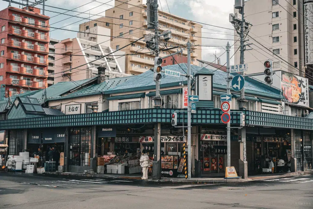 Außenansicht des Nijo Markets in Sapporo, mit traditionellen Marktständen unter einem blauen Dach, umgeben von modernen Wohnhäusern und Straßenkreuzung.