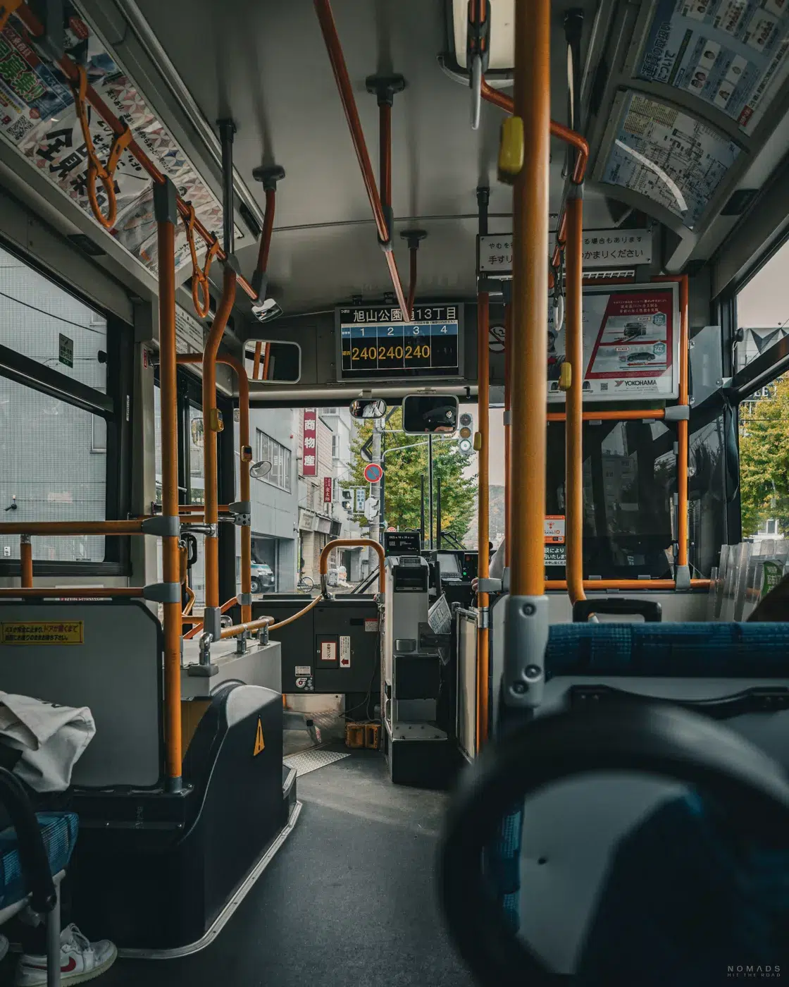 Blick aus dem hinteren Teil eines Stadtbusses in Sapporo mit typischer Ausstattung, Haltestellenanzeige und herbstlicher Straßenszene draußen.