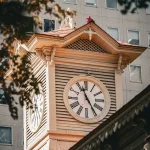 Nahaufnahme des historischen Uhrenturms von Sapporo mit römischen Ziffern, aufgenommen vor moderner Gebäudekulisse.