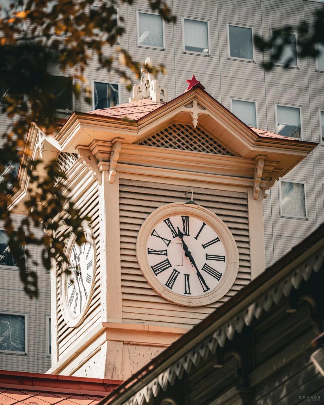 Nahaufnahme des historischen Uhrenturms von Sapporo mit römischen Ziffern, aufgenommen vor moderner Gebäudekulisse.