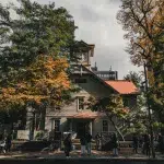 Außenansicht des Sapporo Clock Tower inmitten herbstlicher Bäume, mit Besuchern vor dem Eingang.