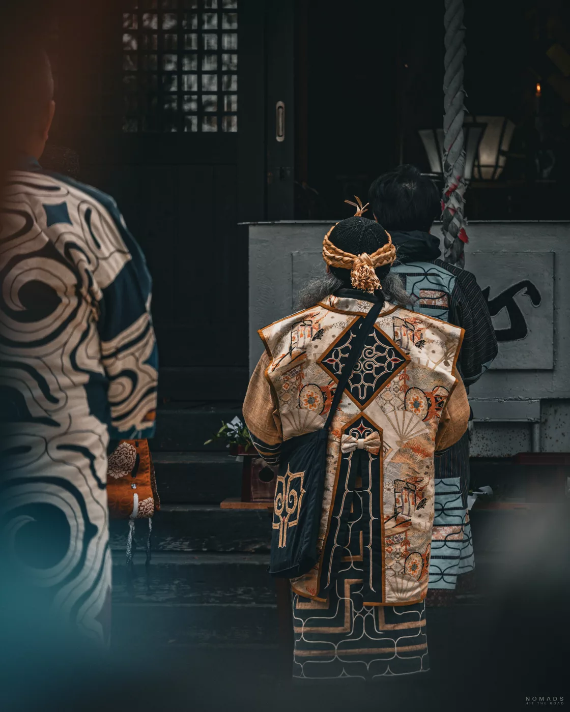 Ainu-Person in aufwendig bestickter Festkleidung steht vor einem Schrein – Moment der Andacht während eines Rituals.
