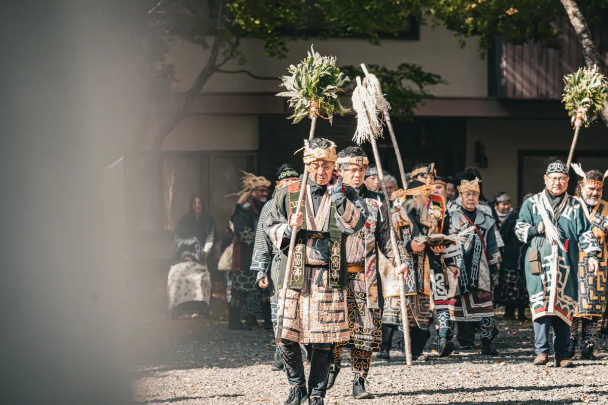 Zeremonielle Ainu-Prozession in traditioneller Kleidung bei einer kulturellen Veranstaltung in Lake Akan, Hokkaido.