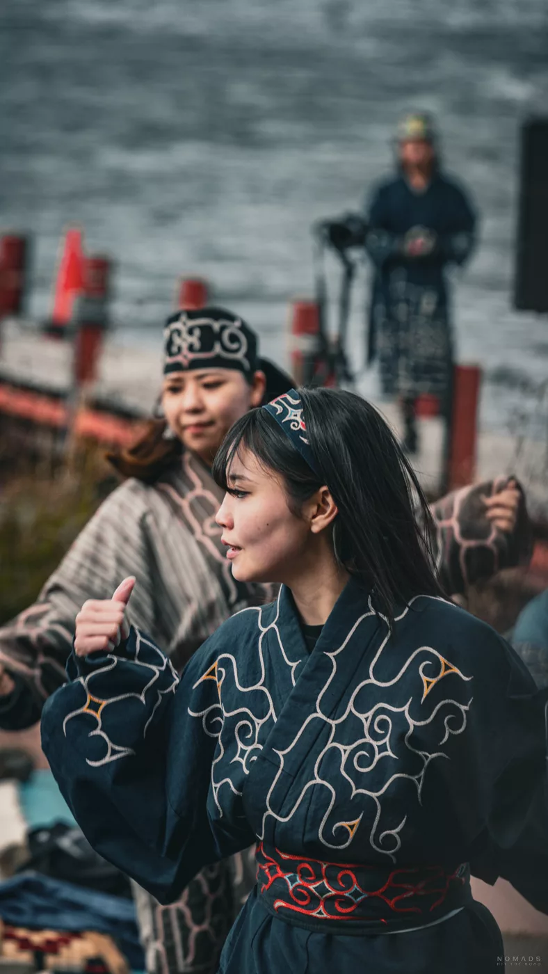 Junge Ainu-Frauen tanzen in traditionellen Gewändern bei einer Zeremonie am Ufer des Lake Akan.