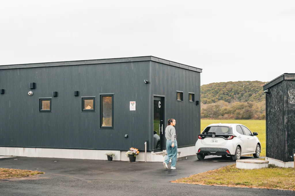 Moderne, freistehende Unterkunft im minimalistischen Stil in Shibecha, Hokkaido, mit angrenzendem Parkplatz vor weiter Naturkulisse.