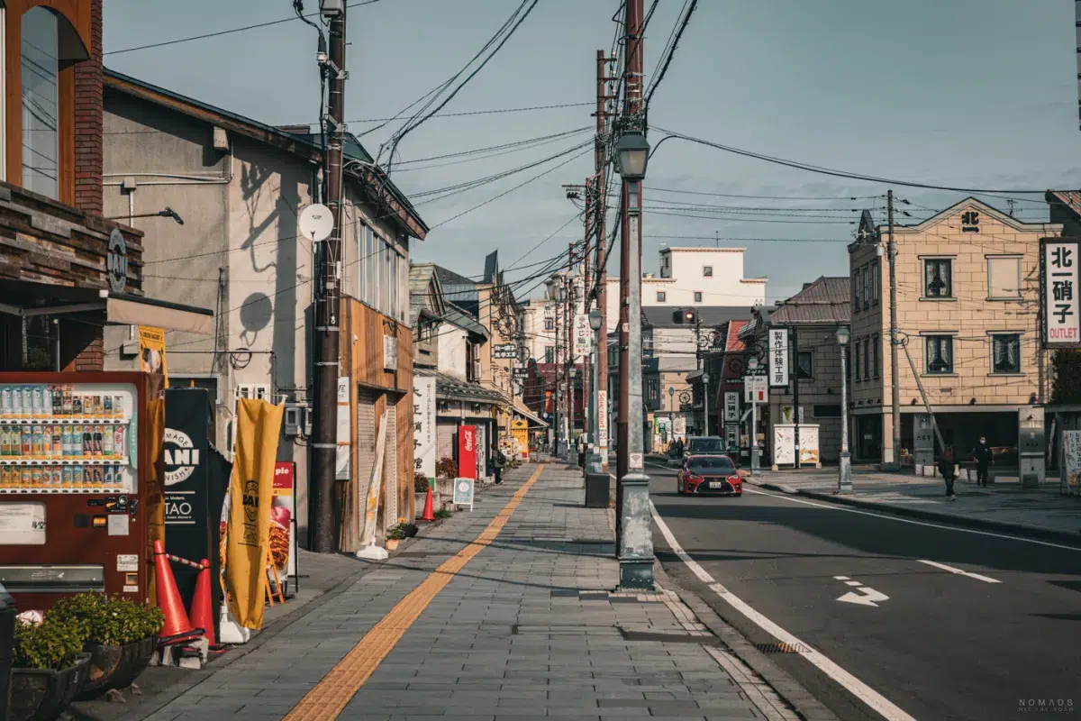 Leere Straße in Otaru am Vormittag, mit kleinen Shops, Automaten und typischen Stromleitungen, bevor die Touristengruppen ankommen.