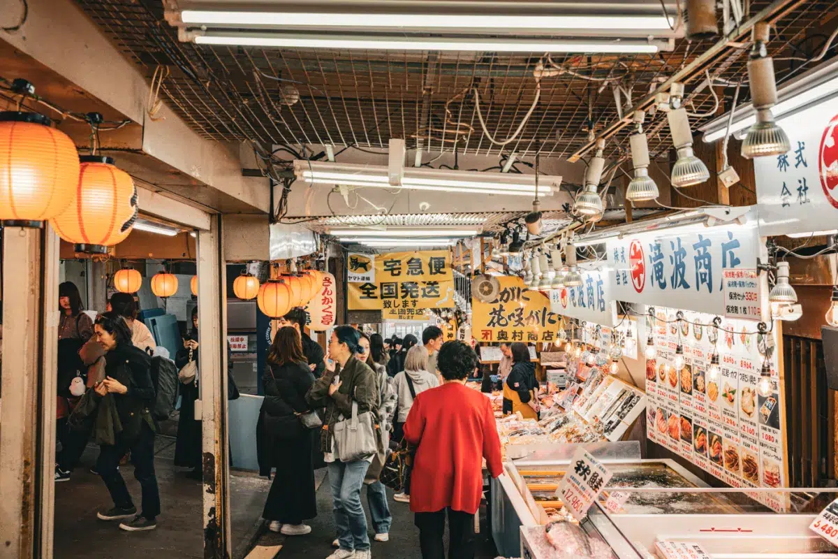Menschen im belebten Innenbereich des Sankaku Market in Otaru, umgeben von Seafood-Ständen, Lampions und japanischen Schildern.