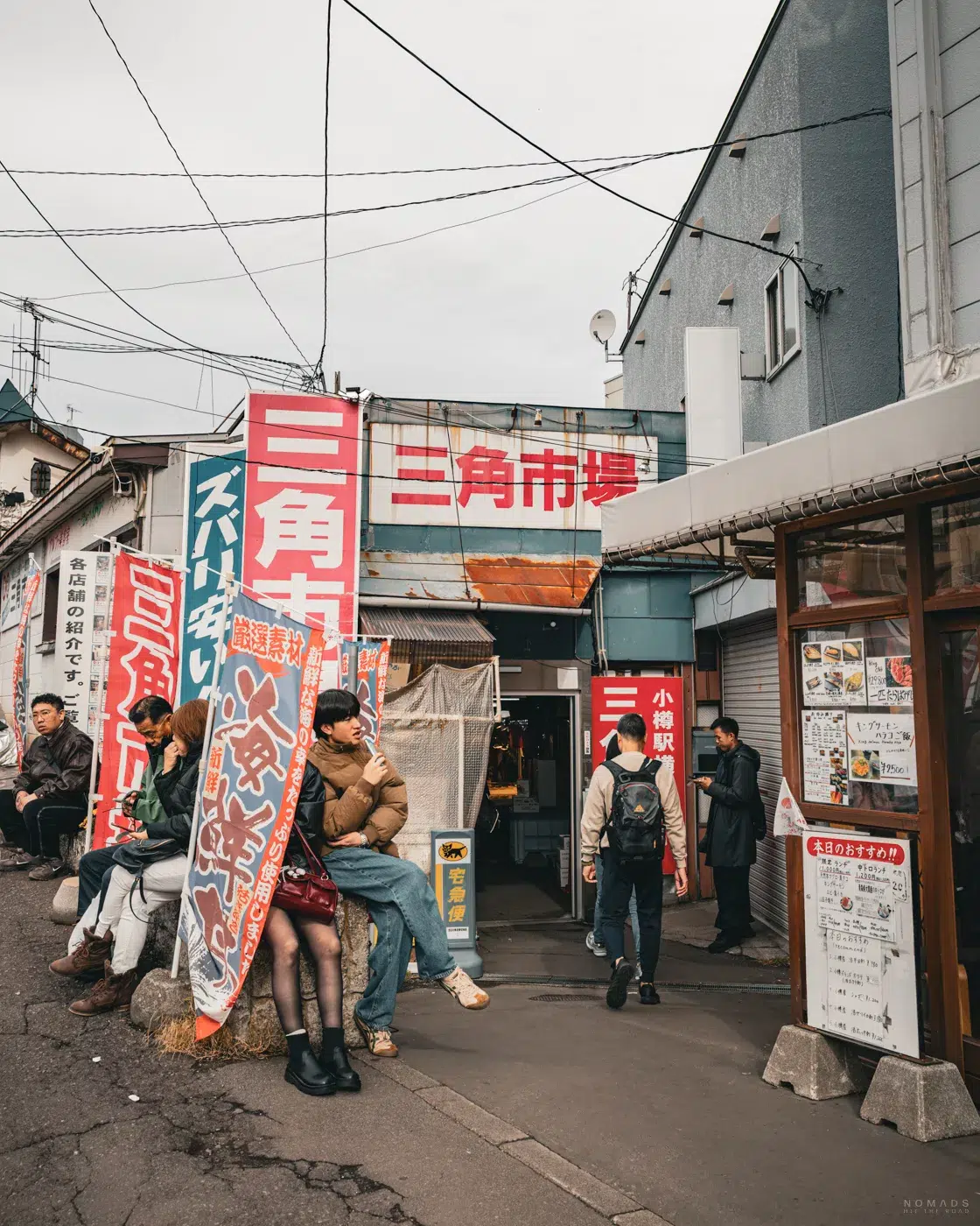 Eingang des Sankaku Market in Otaru mit wartenden Besuchern, Straßenständen und typischen japanischen Werbebannern.