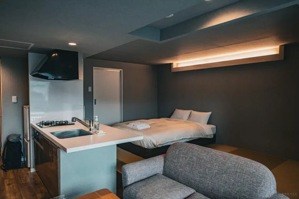 Modernes Apartment im Stay’s OTARU mit Küchenzeile, Sofa und Tatami-Bereich mit Doppelbett – eine praktische Unterkunft für längere Aufenthalte in Otaru.