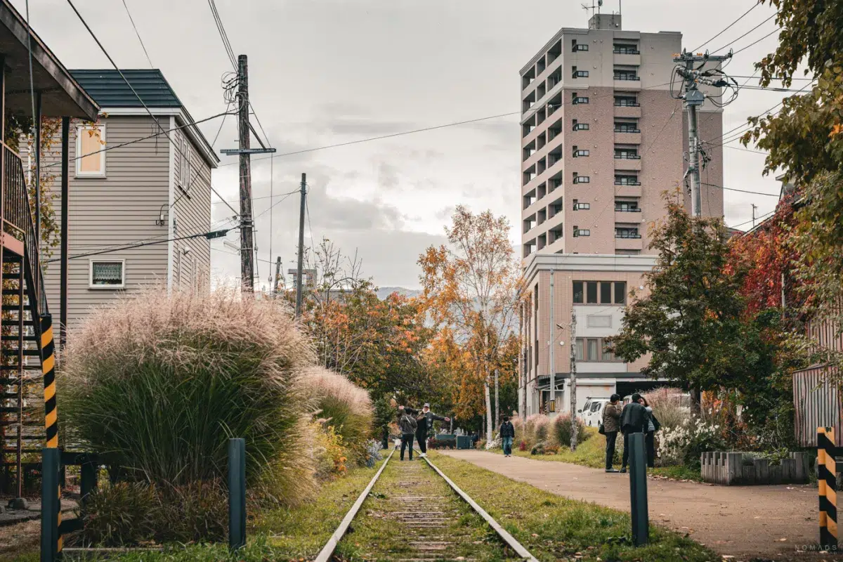 Ehemalige Temiya-Bahntrasse in Otaru im Herbst, mit Gras, Bäumen und Spaziergängern entlang der stillgelegten Gleise.