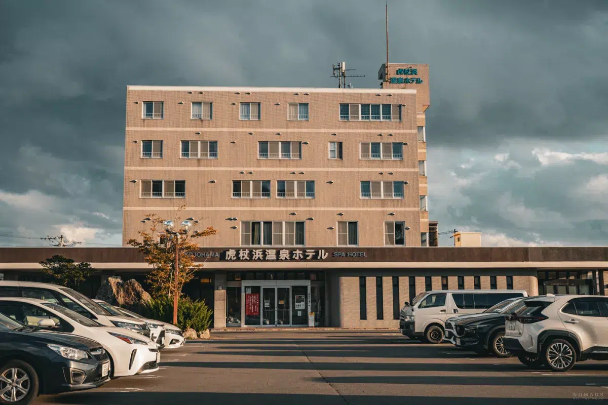Außenansicht des Kojohama Onsen Hotels nahe Noboribetsu mit Parkplatz, vor dunklen Wolken und spätem Nachmittagslicht.