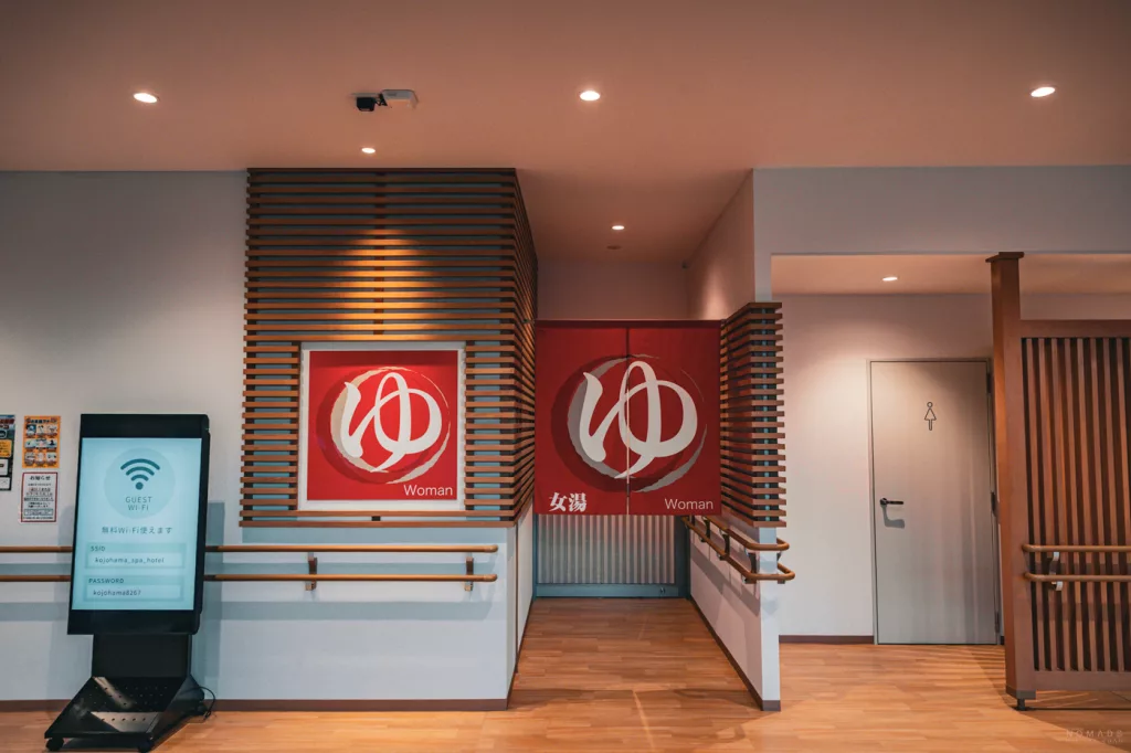 Eingang zum Onsen-Bereich für Frauen in einem japanischen Onsen-Hotel in Noboribetsu, mit roten Vorhängen (Noren), Holzdetails und ruhiger Spa-Atmosphäre.