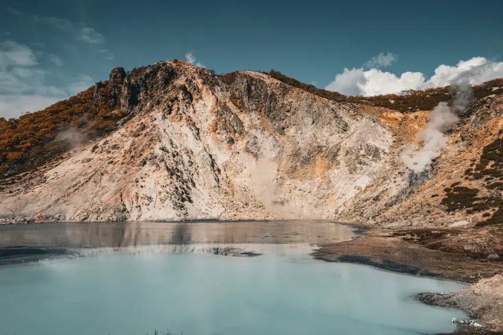 Türkisfarbener Oyunuma-See in Noboribetsu, entstanden aus einem vulkanischen Krater, mit dampfenden Quellen und felsigen Hängen im Hintergrund.