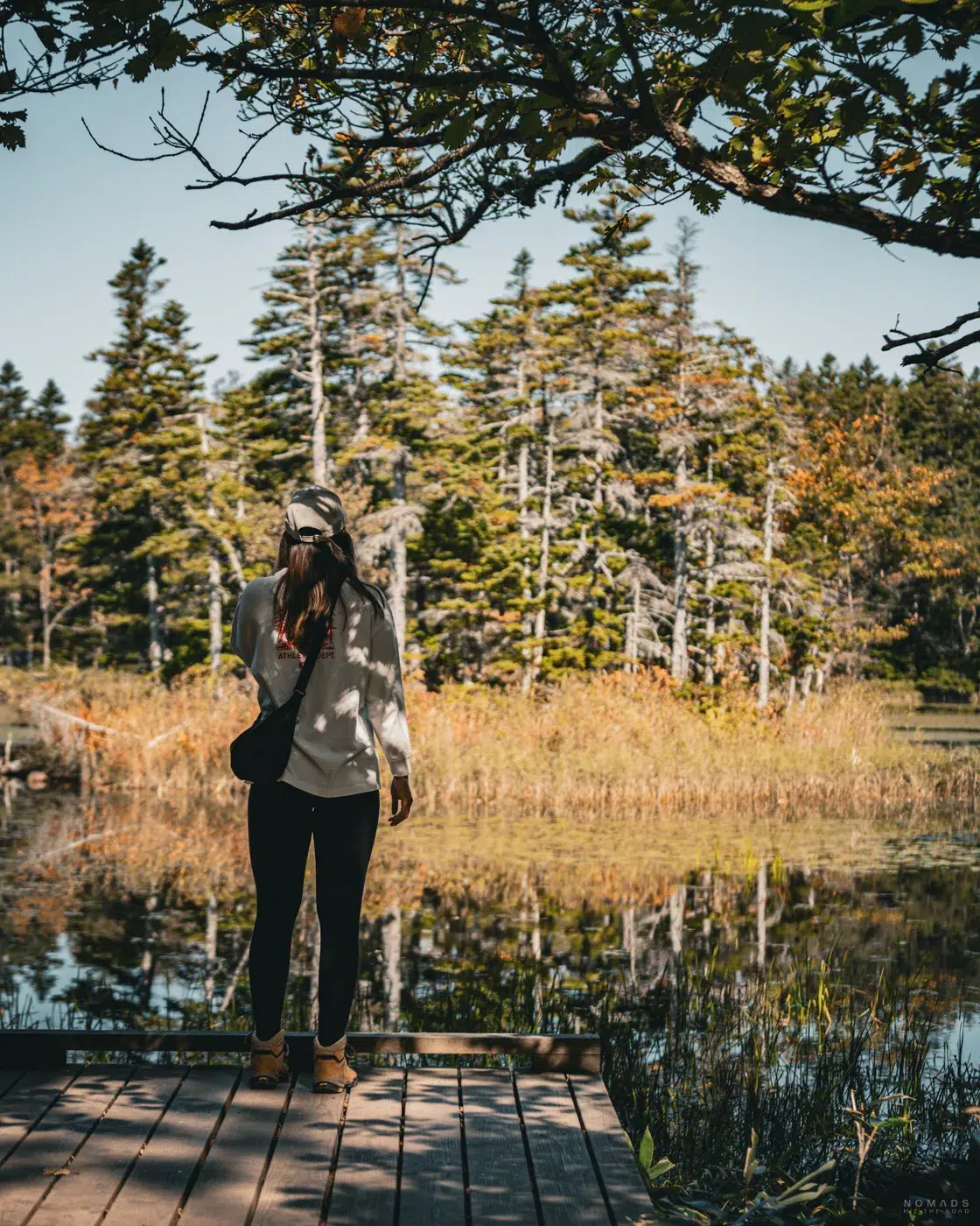 Person steht auf einem Holzsteg an einem der Shiretoko Five Lakes im Herbst, umgeben von herbstlich gefärbtem Wald und spiegelndem Wasser im Shiretoko Nationalpark auf Hokkaido.