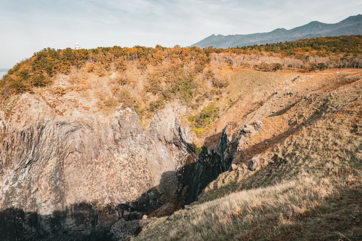 Blick auf die Klippenlandschaft bei den Furepe-Wasserfällen in Shiretoko mit herbstlich gefärbtem Wald und Bergen im Hintergrund.