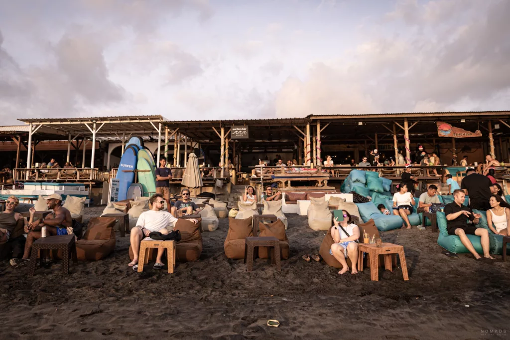 Menschen sitzen in einer Strandbar auf Bali und nutzen Smartphones und Laptops – mobiles Internet unterwegs im Alltag