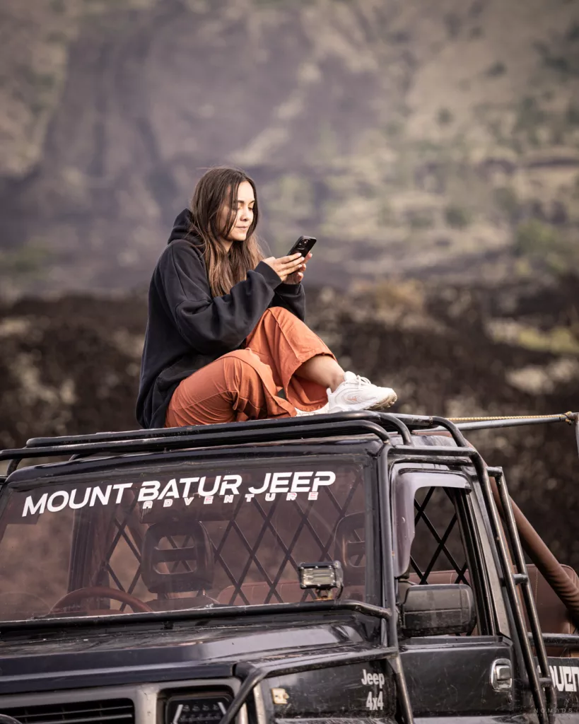 Reisende sitzt auf einem Jeep am Mount Batur auf Bali und nutzt ihr Smartphone. Wichtig für eine gute Verbindung die passende eSim Bali