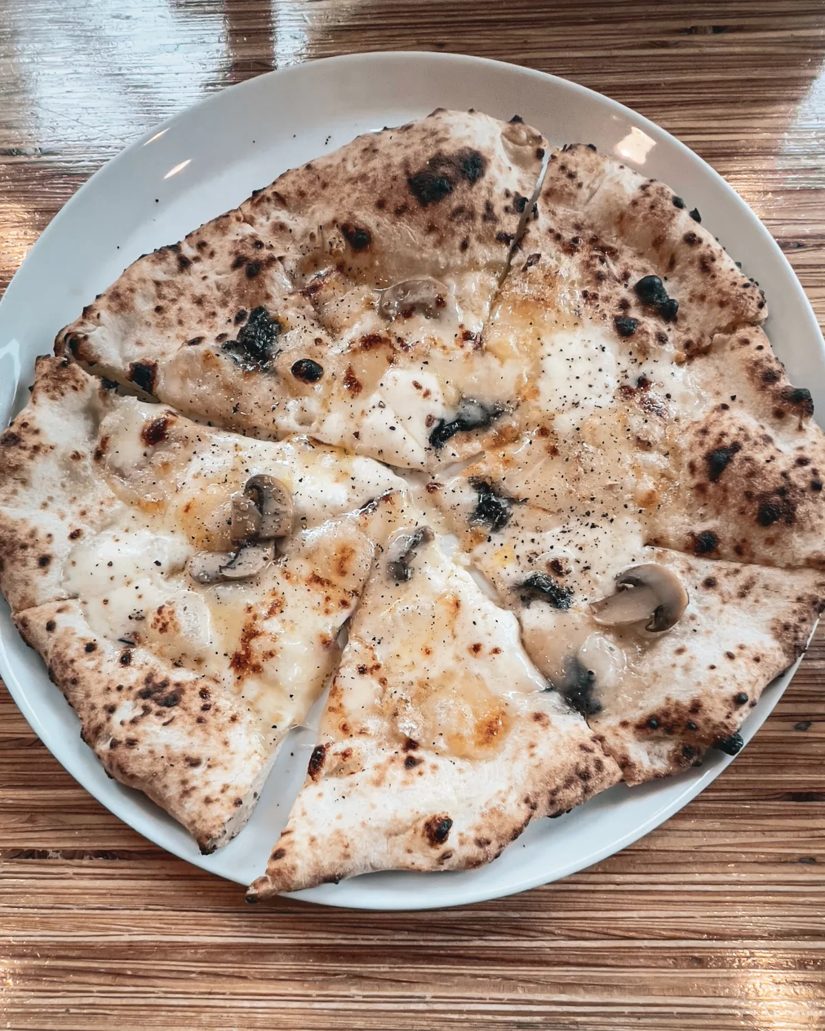 Frisch gebackene Pizza mit geschmolzenem Käse und Champignons, in Stücke geschnitten und auf einem weißen Teller serviert.