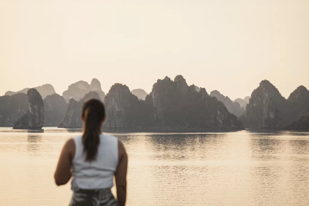 Frau blickt auf die Halong Bay mit ihren Felsformationen bei Sonnenuntergang