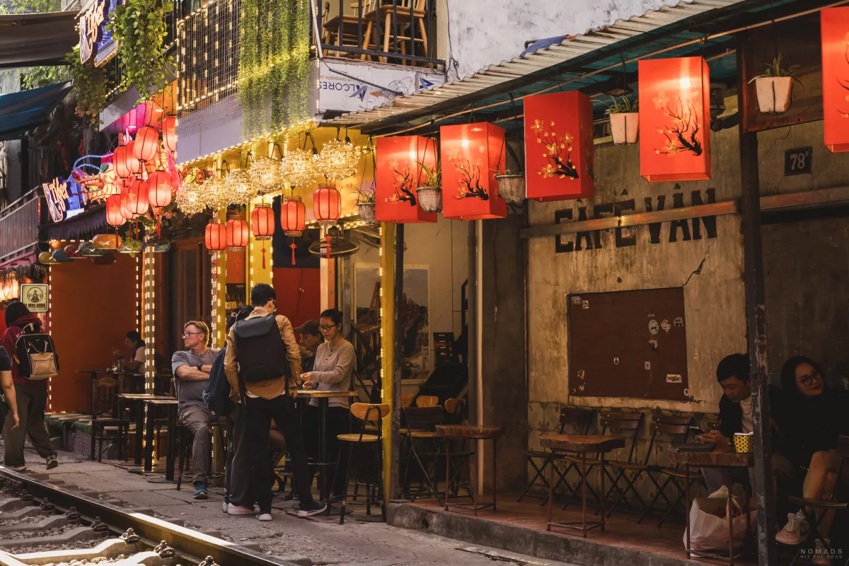 blick auf ein Café, wovor Sitzplätze und Menschen sind, dekoriert mit Lampen