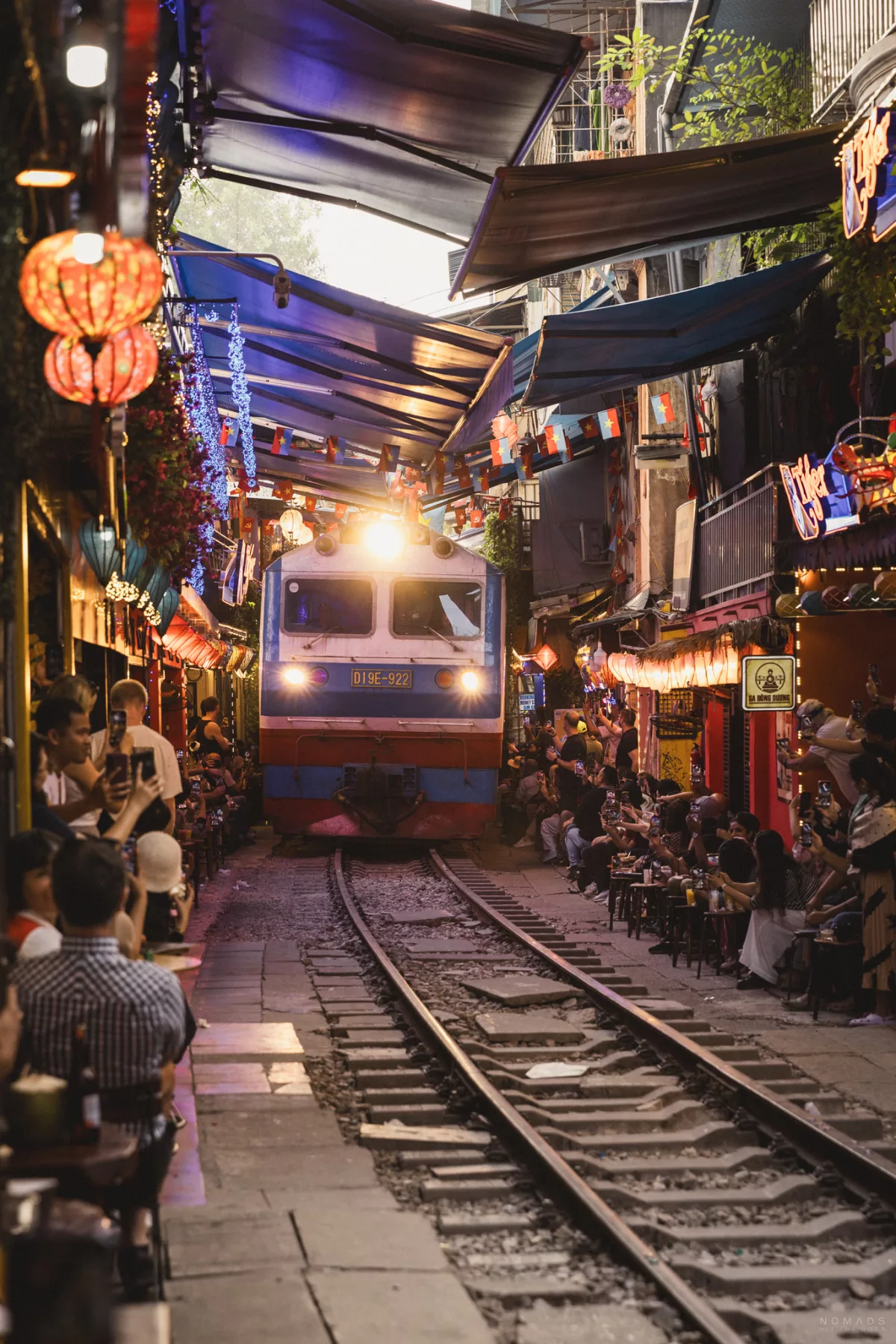 Zug fährt auf einer Gleise auf der Hanoi Train Street während rechts und links Menschen in Cafés sitzen