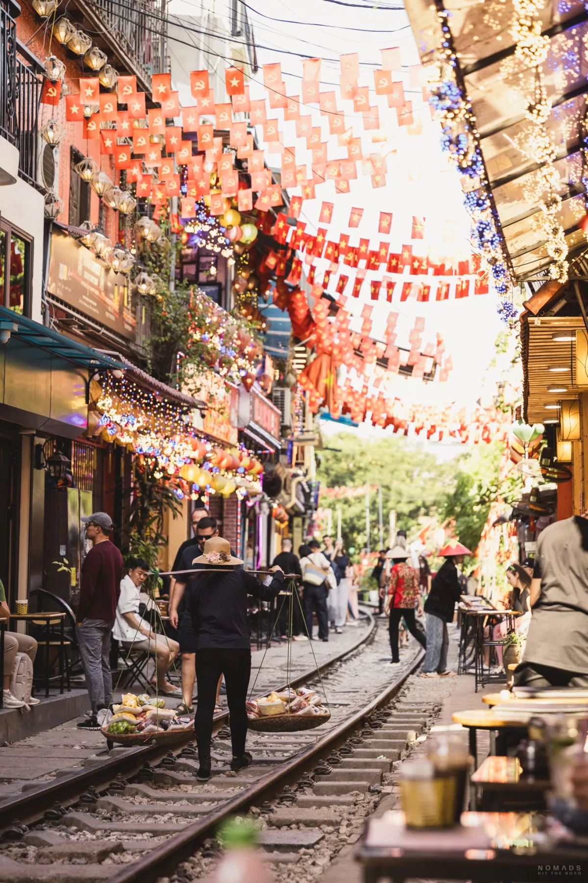 Verkäuferin mit Obst läuft entlang der Hanoi Train Street, die mit Fahnen dekoriert ist