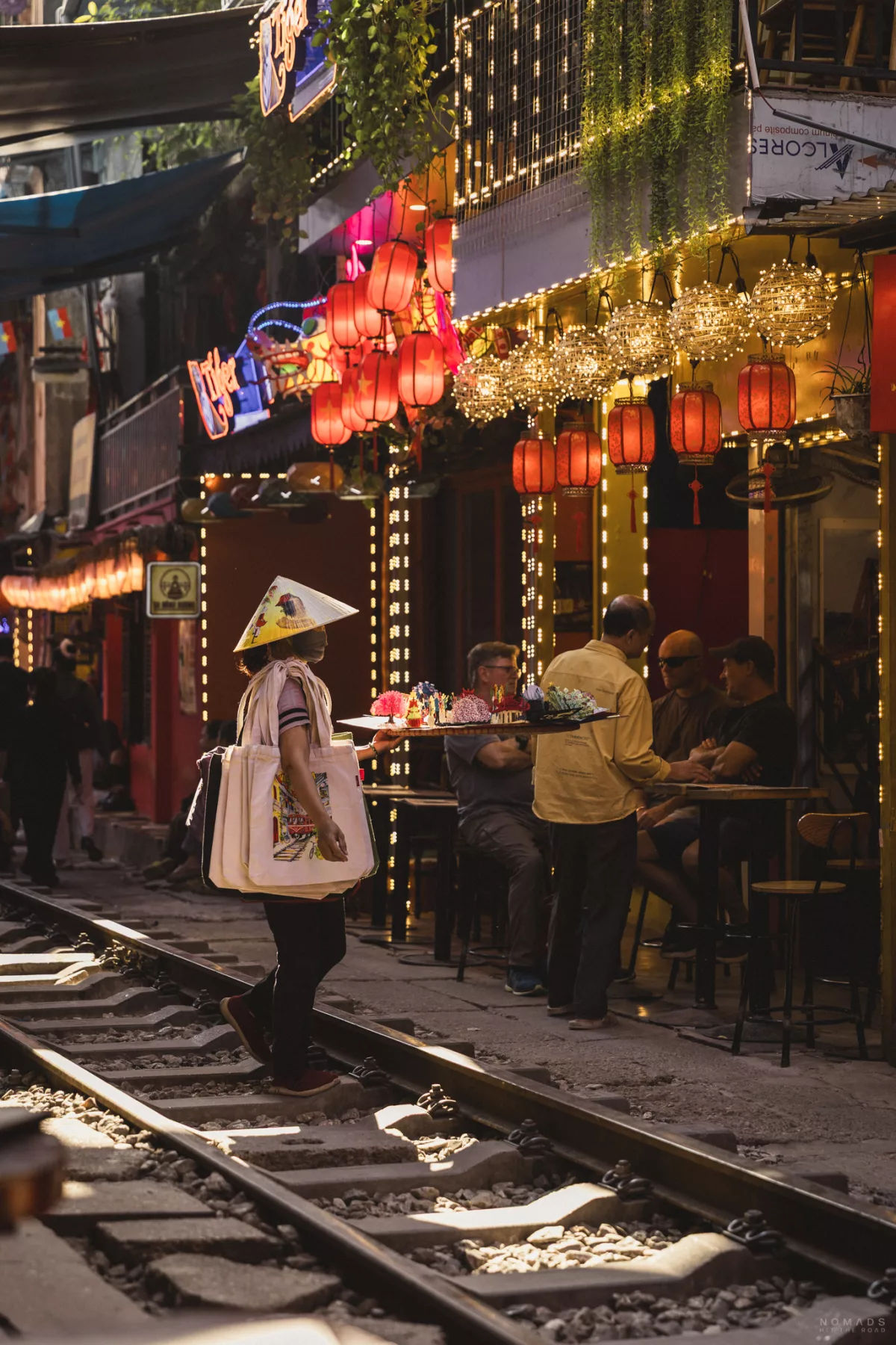 Händlerin mit Grußkarten steht auf der Gleise auf der Hanoi Train Street vor einem Café mit Lampen