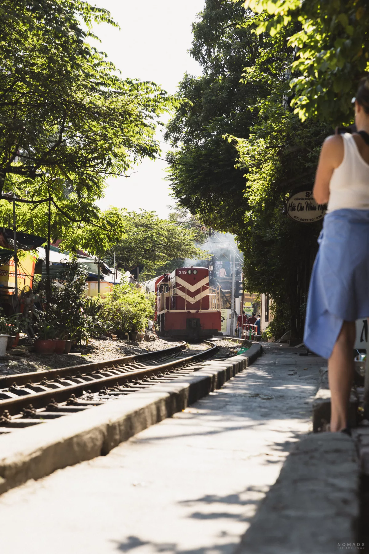 Zug fährt auf einer Gleise, Frau steht am Rand und macht ein Foto