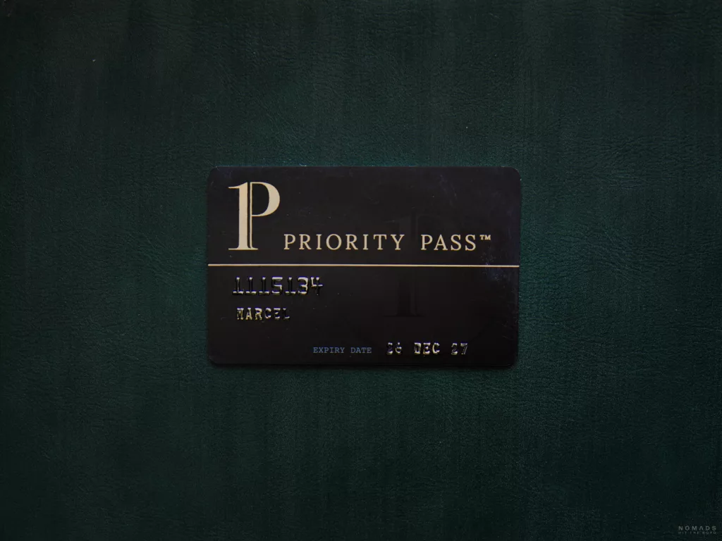 Eine schwarze Priority Pass Mitgliedskarte mit goldener Aufschrift, die flach auf einer dunkelgrünen, lederartigen Oberfläche liegt.
