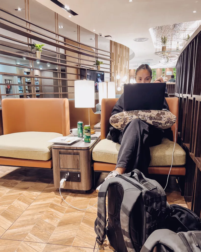 Eine komfortable Arbeitsecke in einer Priority Pass Lounge, ausgestattet mit Polstersesseln, Beistelltisch und integrierten Ladestationen für Laptop und Smartphone.