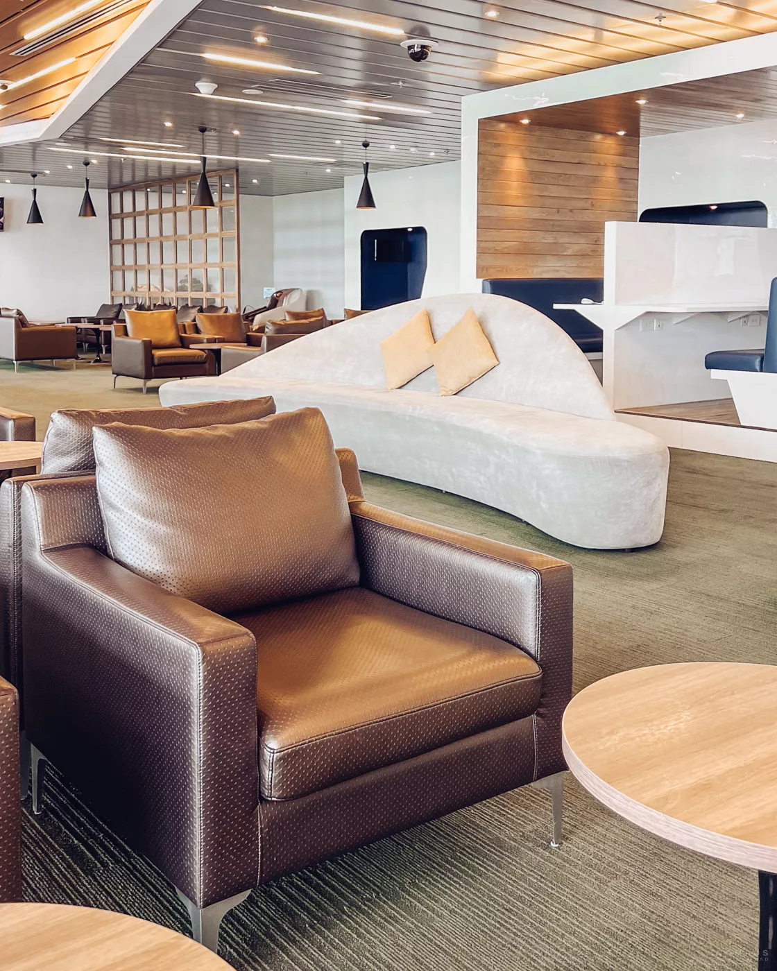 Ein eleganter Loungebereich mit dunklen Ledersesseln und einem langen, weiß glänzenden Buffet, das verschiedene warme Mahlzeiten bereithält.