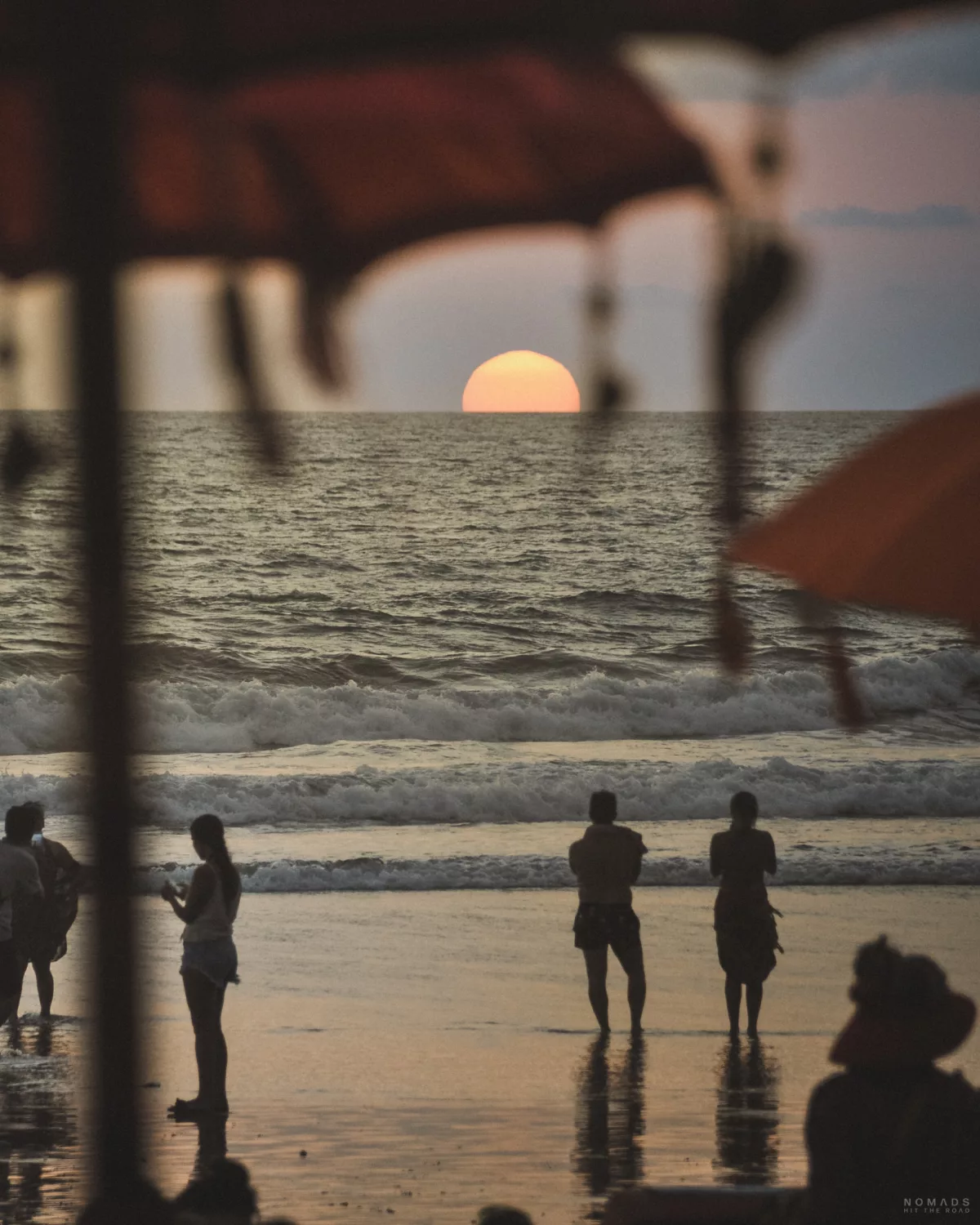 Sonnenuntergang am Strand mit Menschen am Meer und Sonnenschirmen auf Bali