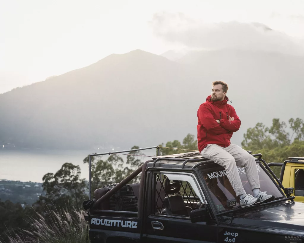 Mann in roter Jacke sitzt auf einem Autodach vor dem Mount Batur in Kintamani