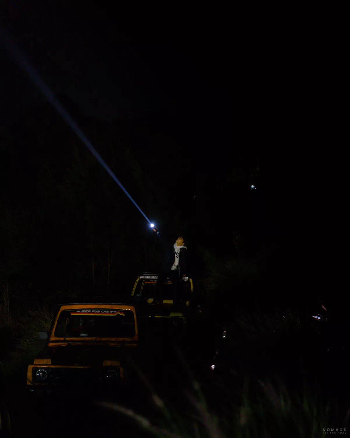 Mann leuchtet mit einer Taschenlampe in den dunklen Himmel und sitzt auf einem Jeep